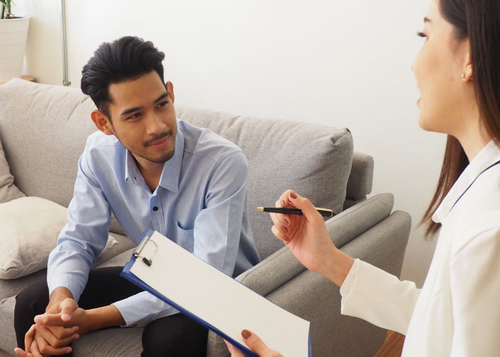 man sits on a couch and listens to a woman with clipboard taking notes and talking