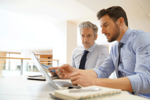 two men sit at table with a laptop in front of them discussing consulting services for behavioral health treatment centers