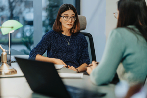 woman with glasses sits with another woman in a meeting discussing consulting services for substance abuse treatment centers